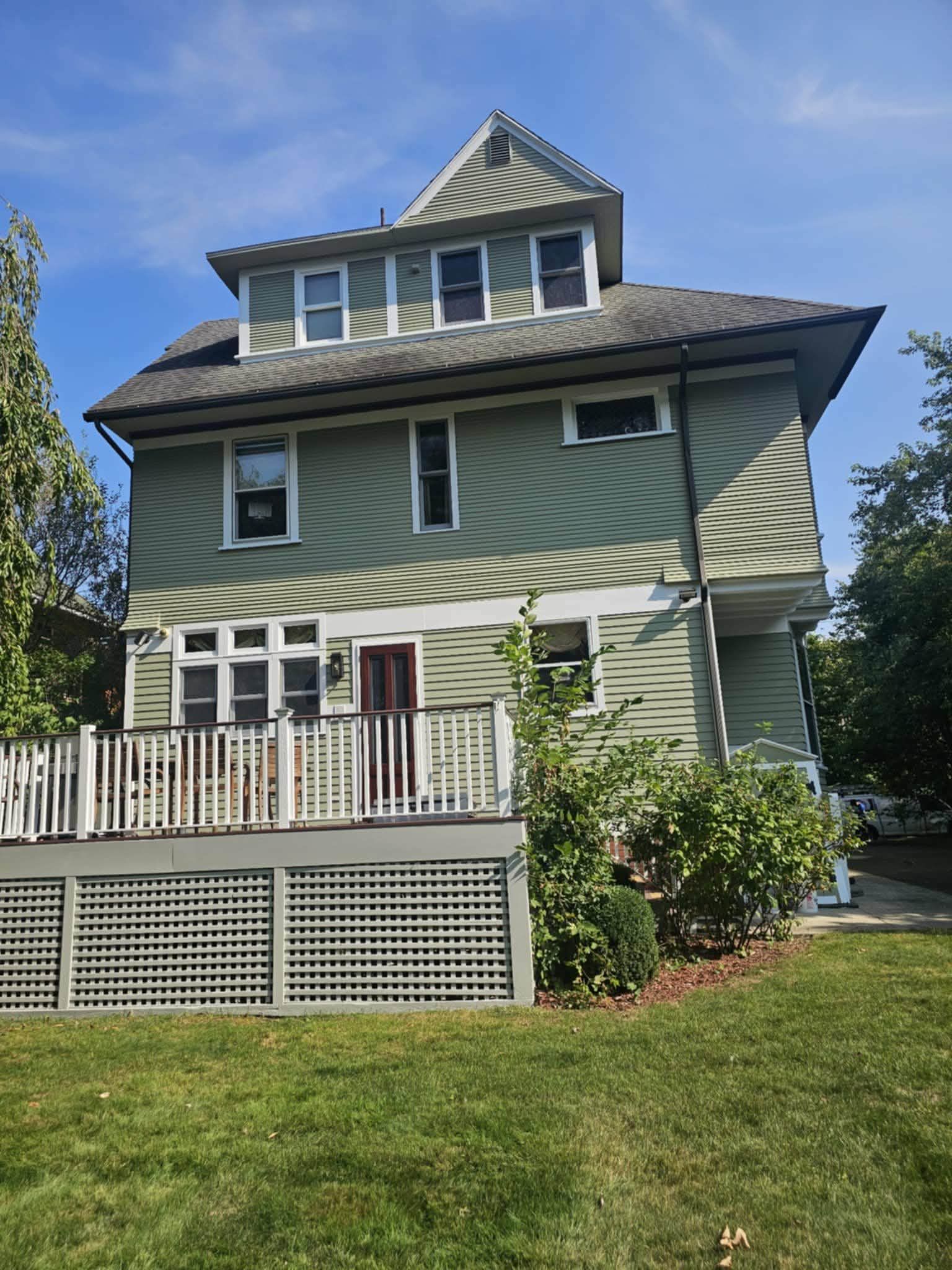 Three-story house freshly repainted in sage green with white trim and a white porch railing